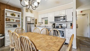 Une cuisine moderne avec des meubles blancs, un réfrigérateur en acier inoxydable, un four à micro-ondes et une cuisinière. On y trouve une table à manger en bois avec six chaises.