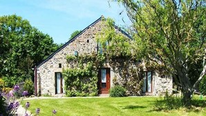 A stone building with a gabled roof, a central entrance, and a small porch area. - A 1 bedroom cottage that sleeps up to 4 with heated covered pool (Henansal)