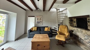 A living room with a sofa, a wooden coffee table, a yellow armchair, a fireplace, and a spiral staircase. - A 1 bedroom cottage that sleeps up to 4 with heated covered pool (Henansal)