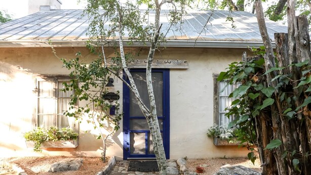 A small building with a blue door, a stone pathway, and a tree in front.