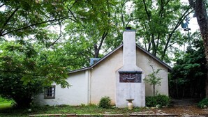 A rustic building with a chimney, surrounded by lush greenery.