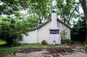 Surrounded by lush greenery, this charming building features a traditional design with a prominent chimney and a small window.