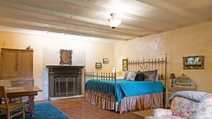 A bedroom with a bed, a chair, a desk, and a fireplace.