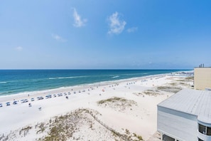 A beach with white sand, a clear blue sky, and a building with a flat roof. - Coastal Beachfront Condo w/ Pool & Sauna | Gulf Views | Sleeps 6 (Gulf Shores)