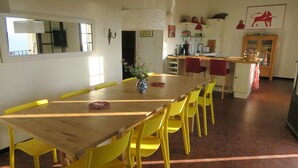 Un comedor con una mesa de madera y sillas amarillas, un florero con flores, y una cocina al fondo.