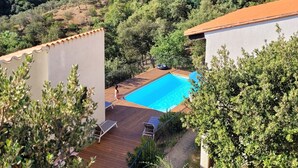 Un área de piscina con cubierta de madera, rodeada de follaje y montañas al fondo.