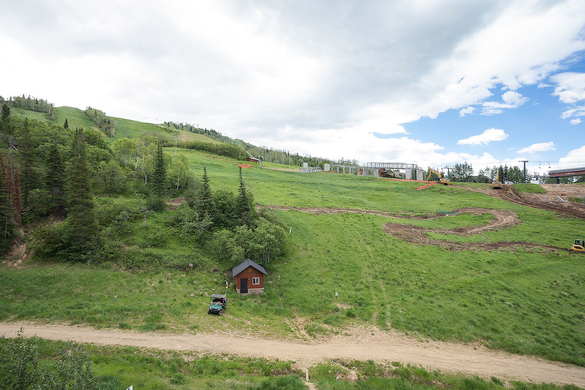 Un paysage rural avec une petite cabane, un chemin de terre et du matériel de construction.