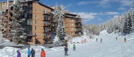 A ski resort with multi-story buildings, snow-covered trees, and skiers on the slopes.