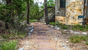 Un sendero de piedra que lleva a una escalera de madera y un edificio de piedra con una ventana y un cartel.