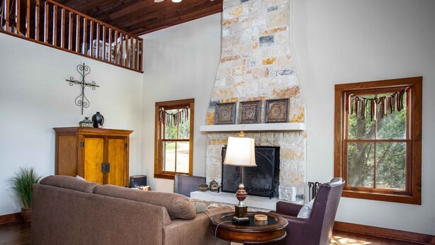 Amplia sala de estar con chimenea de piedra, vigas de madera y ventanas grandes.