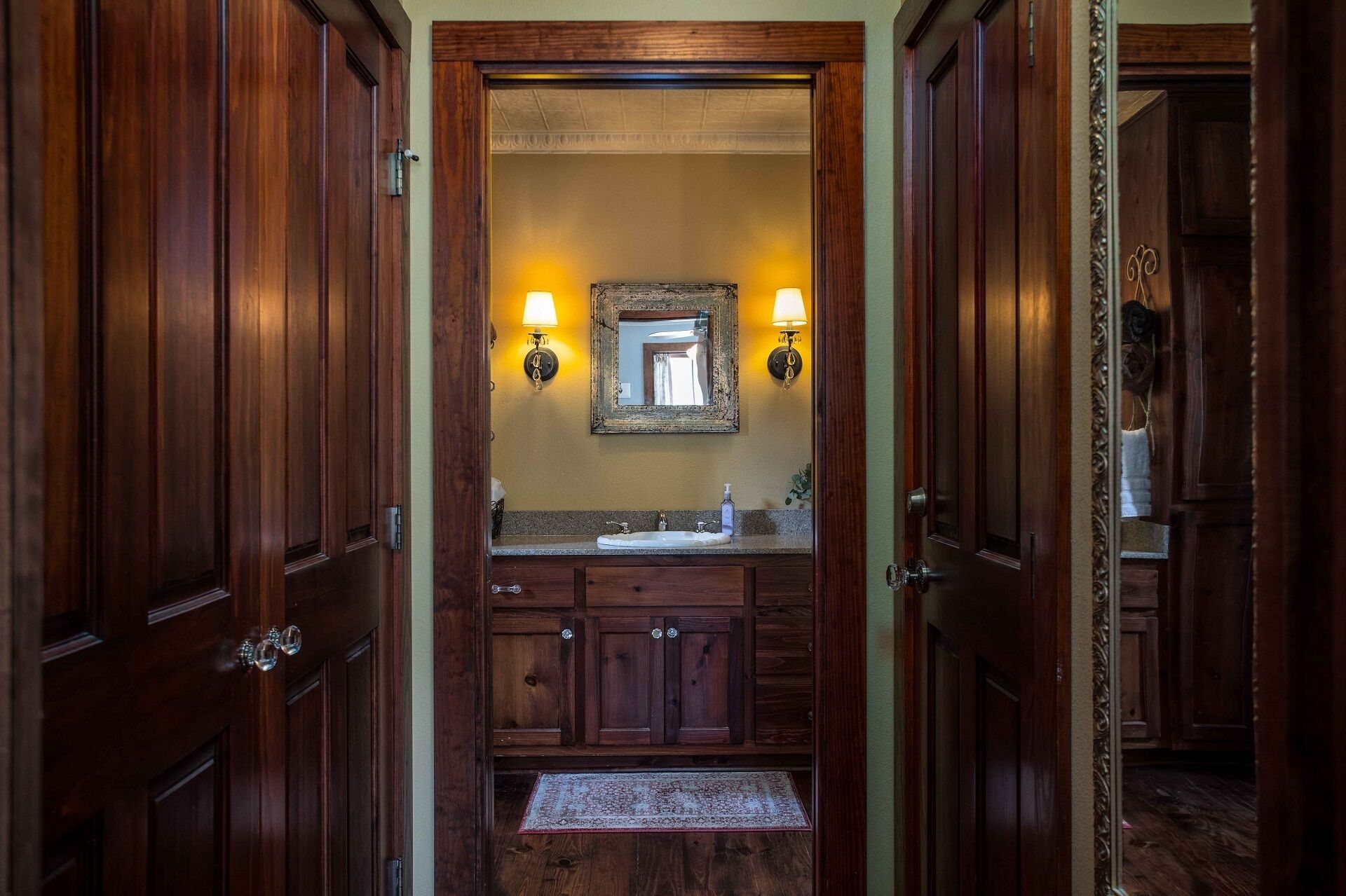 A wooden bathroom with a sink, two wall-mounted lights, and a mirror.
