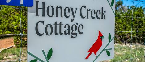 Señal para Honey Creek Cottage, con diseño de aves cárdinal y follaje.