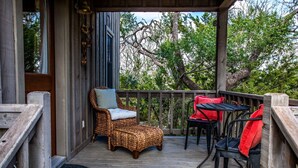 Un espacio al aire libre cubierto con una silla de mimbre y una mesa, rodeado de una terraza de madera y árboles.