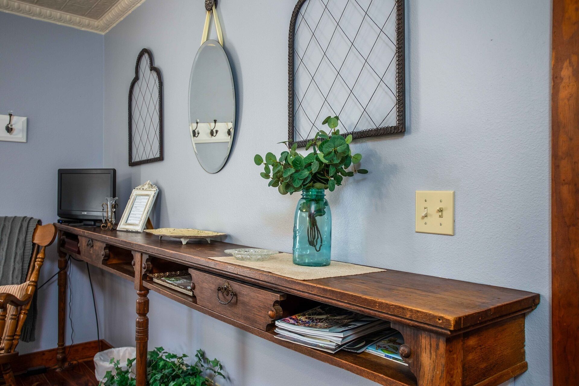 A wooden desk with a vase of green plants, a television, and a wall-mounted mirror.