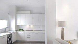 A modern kitchen with white cabinets, a built-in washing machine, and a dining area with a table and chairs. - iloftmalaga Císter Estudio (Málaga)