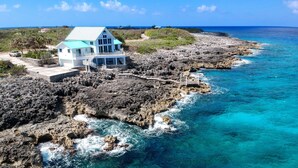Una casa costera con balcón que da a terreno rocoso y aguas azules cristalinas.