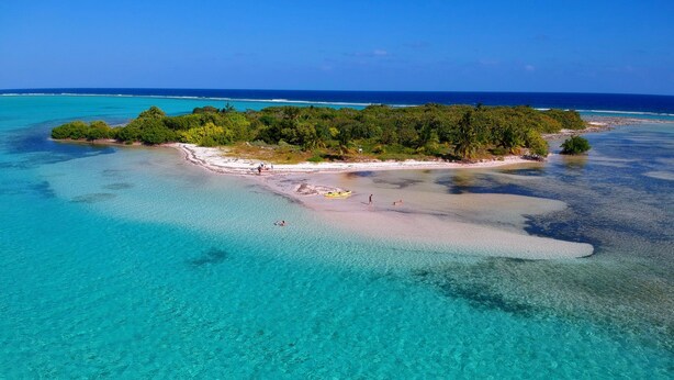 Vista aérea de una isla tropical con aguas turquesas cristalinas, una playa arenosa y densa vegetación verde.