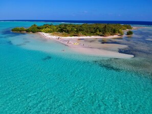 Vista aérea de una isla tropical con aguas turquesas cristalinas, una playa arenosa y densa vegetación verde.