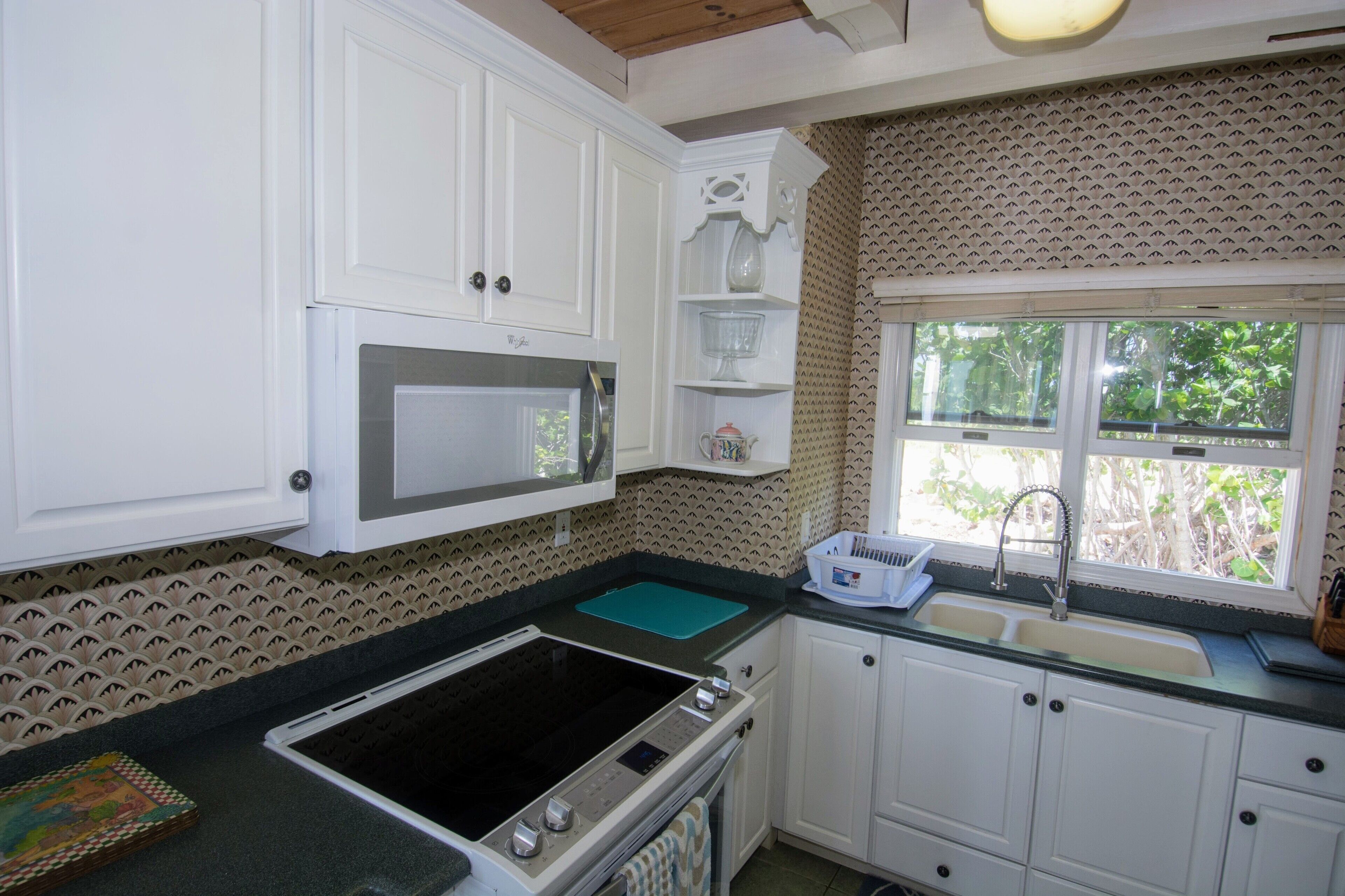 A kitchen with white cabinets, a microwave, a stove, and a window with a view of greenery.