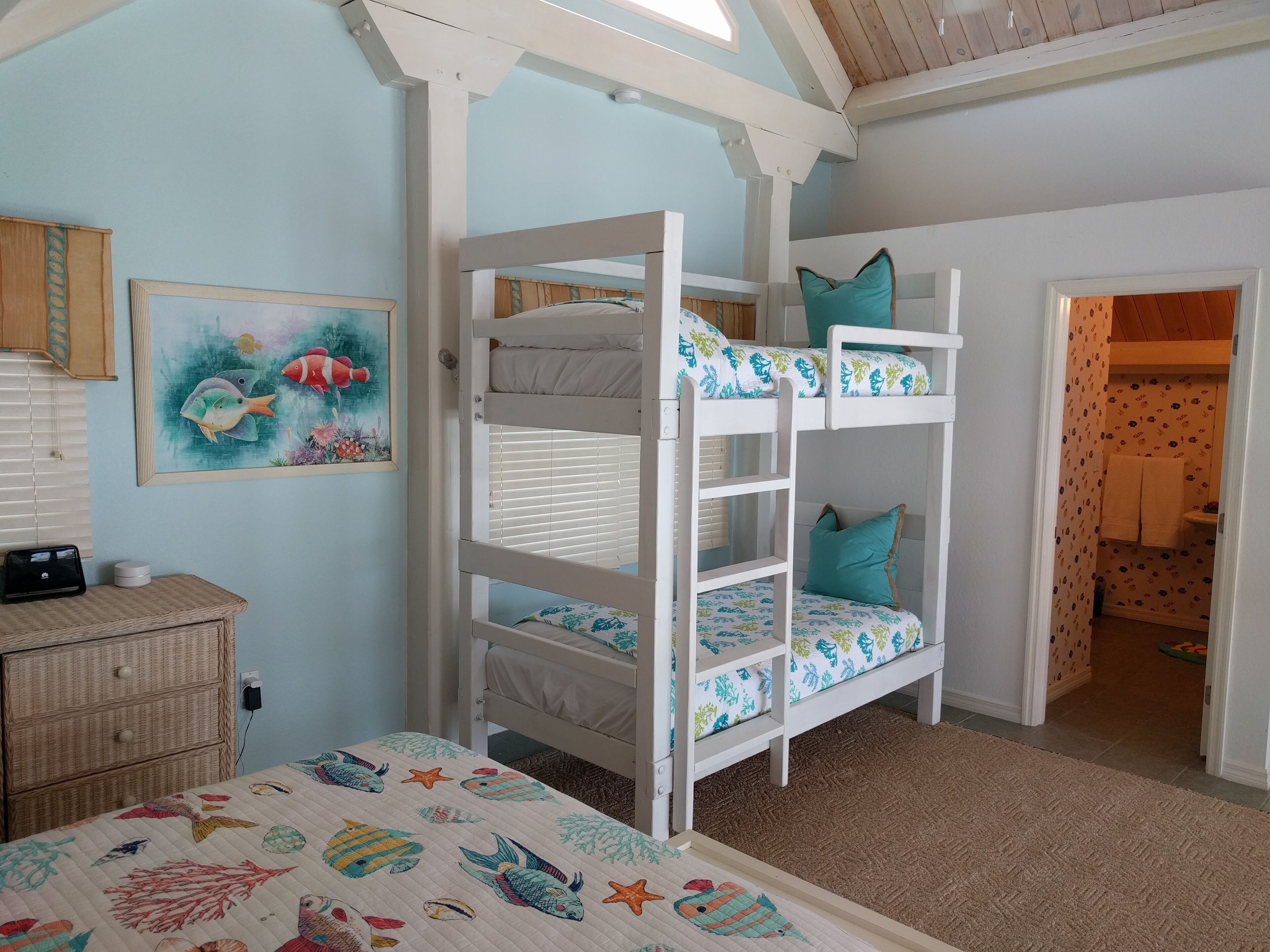Un lit superposé avec un lit inférieur, une table de chevet, une commode et un mur orné d’un tableau encadré.
