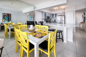 A modern kitchen with a central island, yellow chairs, and a glass dining table.