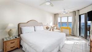Ein Hotelzimmer mit einem großen Bett, einem Nachttisch mit Lampe, einem Sessel und Blick auf das Meer durch große Fenster.