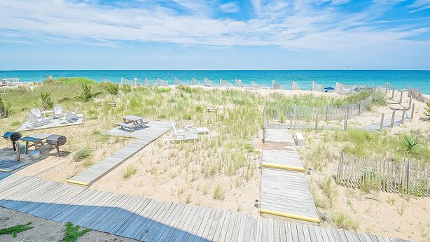 A beach with a wooden boardwalk, beach chairs, and a barbecue area.