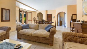 Ein gemütliches Wohnzimmer mit einem Rattan-Sofa, einem Essbereich mit Tisch und Stühlen sowie einer Küchenzeile mit Arbeitsplatte und Schränken.