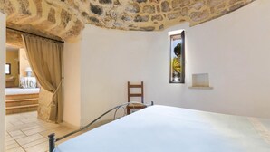 Ein Schlafzimmer mit Steindecke, einem Bett, einem Fenster und einem Sessel.