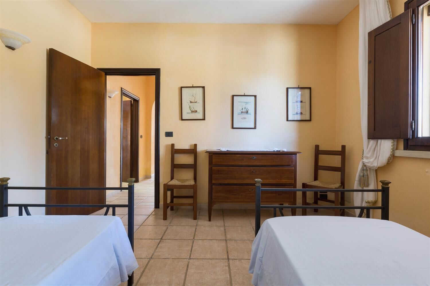 A room with two beds, a desk, and chairs, with a door leading to another room.