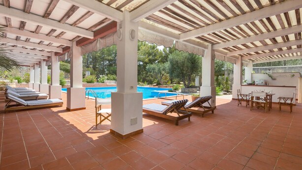 Ein überdachter Außenbereich mit Pool, Liegestühlen und einer Bar.