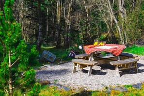 A picnic table with a red checkered tablecloth, surrounded by a forested area. - Raasay Lodge (Birchbrae, Onich, Nr Fort William)