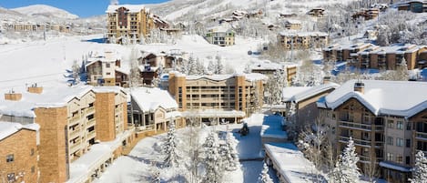 A snow-covered resort with multiple buildings, including a large hotel with a ski lift visible in the background.