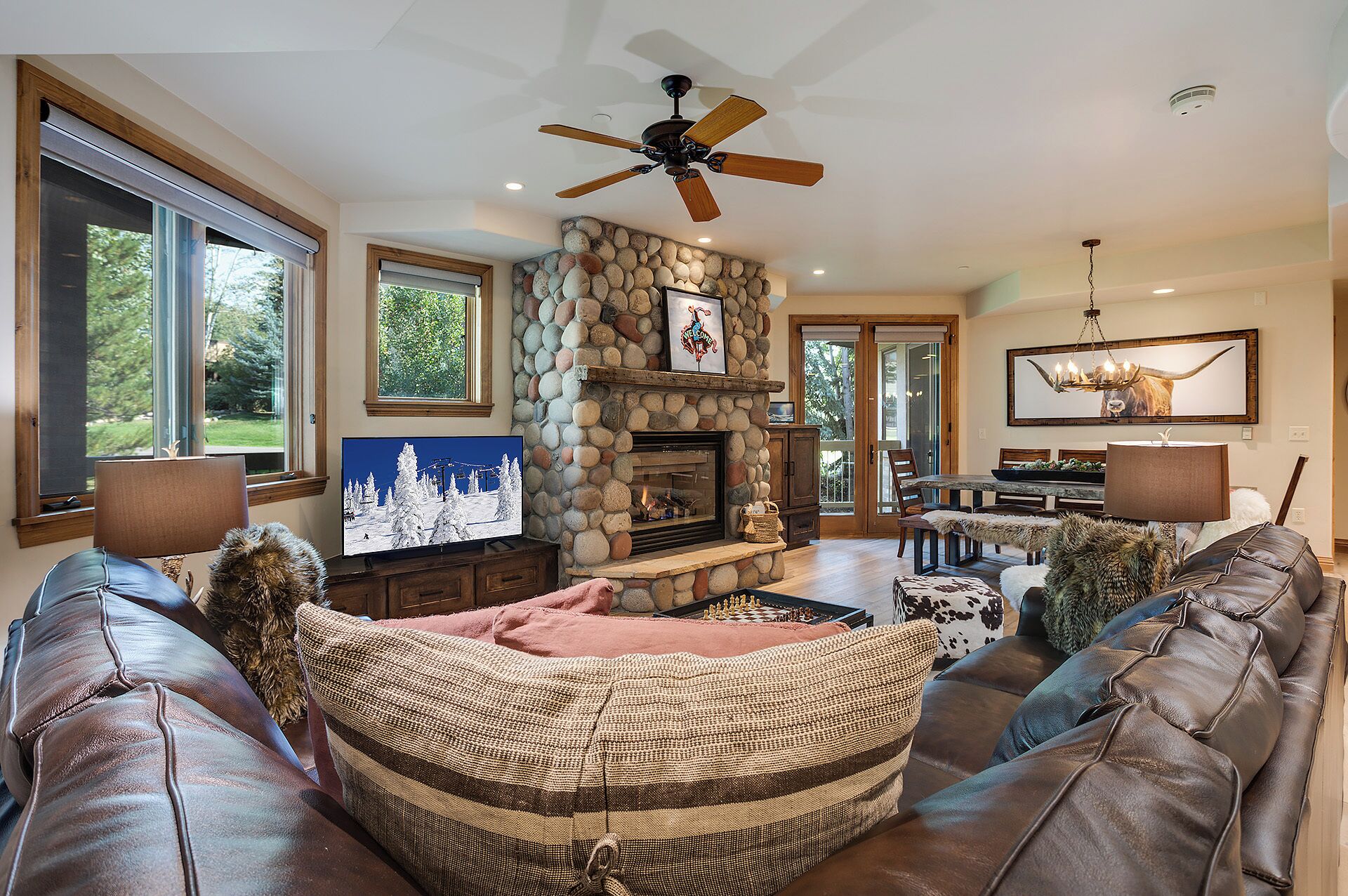 A spacious living room with a stone fireplace, leather sofas, a television, and a dining area with a chandelier.