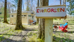 Puinen kyltti, jossa lukee ”Evergreen”, on sijoitettu leirintäalueelle. Taustalla on pieni mökki, puita ja ulkokalusteita.