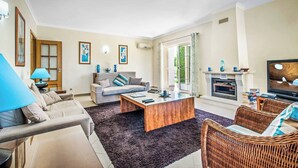 A living room with a sofa, coffee table, and wicker chairs. There is a fireplace with a TV, and a window with curtains. - Villa Altair - Four Bedroom Villa, Sleeps 8 (Casa Altair Joinal)
