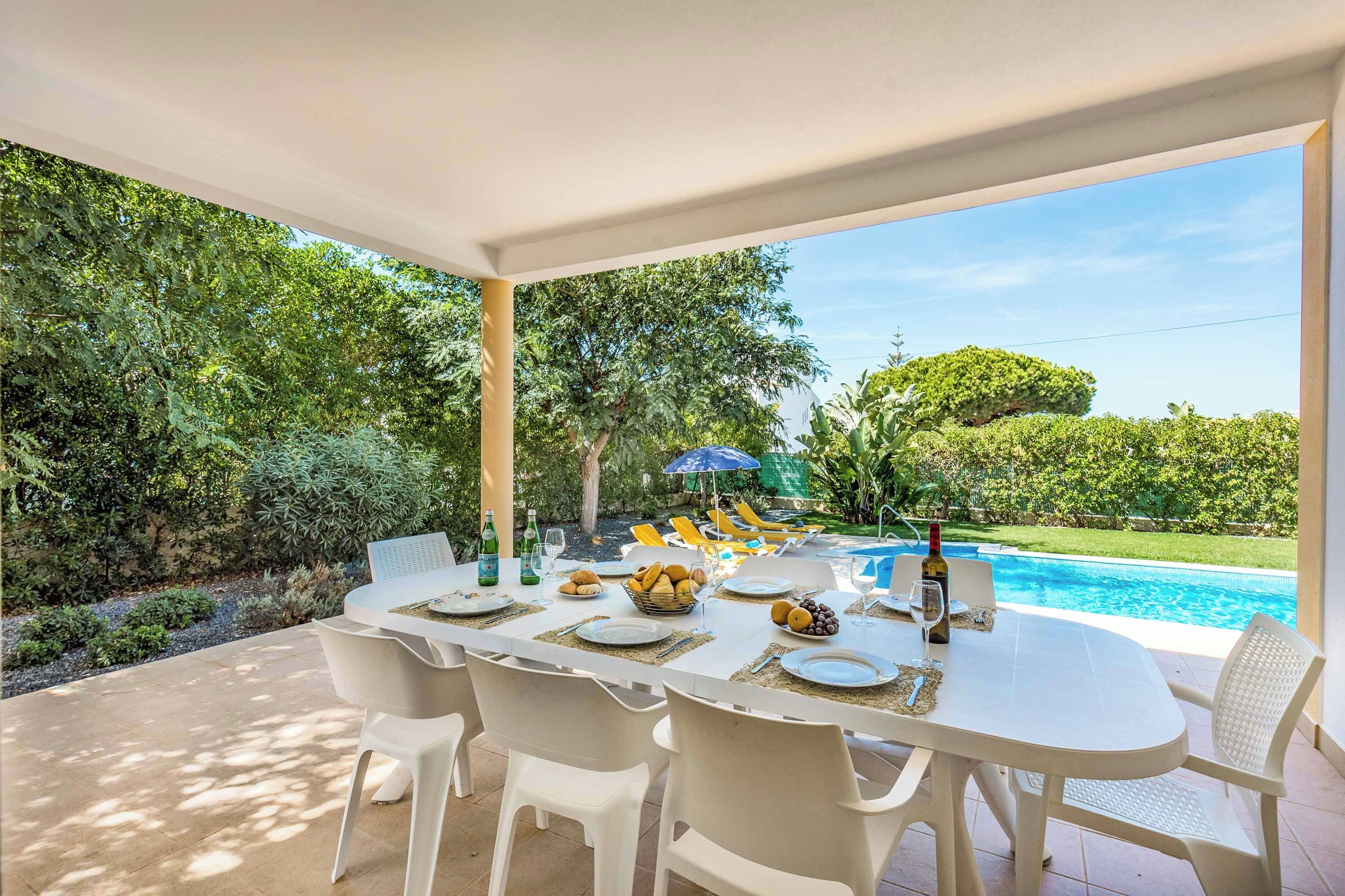An outdoor dining area with a pool view, white furniture, and a clear sky.