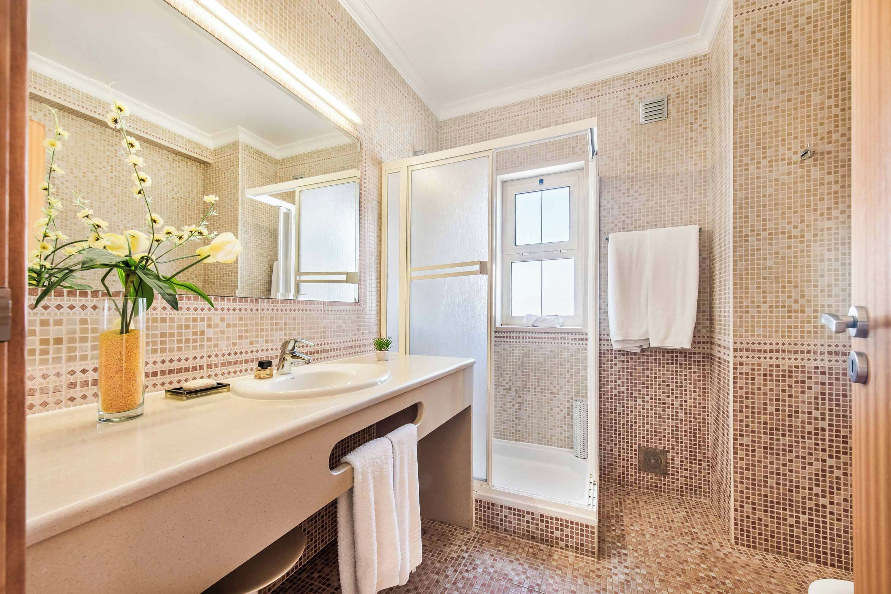 Une salle de bain avec un grand miroir, un lavabo, une douche et un sol carrelé.