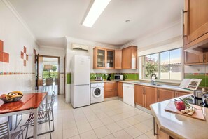A modern kitchen with a washing machine, microwave, and a dining area with chairs and a table. - Villa Altair - Four Bedroom Villa, Sleeps 8 (Casa Altair Joinal)