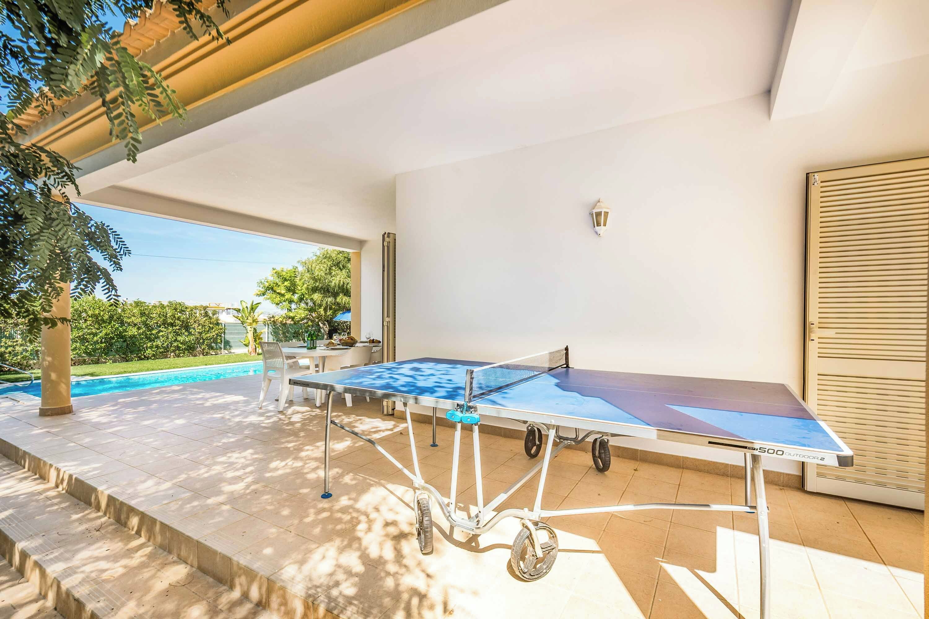 Ett bordtennisbord för utomhusbruk med hjul, ett bord och några stolar, och utsikt över en swimmingpool.