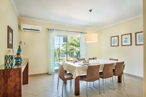 A dining area with a table set for six, surrounded by chairs, a hanging light fixture, and a view of greenery outside. - Villa Altair - Four Bedroom Villa, Sleeps 8 (Casa Altair Joinal)