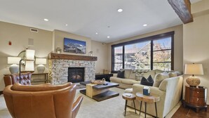 A living room with a stone fireplace, leather armchair, and a large window with blinds.