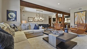 A modern living room with a sofa, armchairs, and a coffee table. There are framed pictures on the wall and a painting on the right.