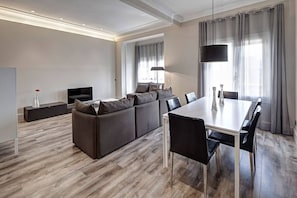 A modern living room with a sofa set, a dining table with chairs, a TV, and a lamp.
