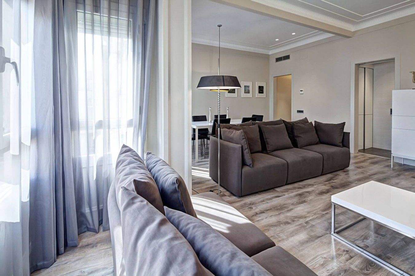 A modern living room with a sectional sofa, a dining area, and a kitchen in the background.