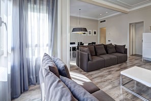 A modern living room with a sectional sofa, a dining area, and a kitchen in the background.