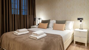 Una cama bien hecha con una colcha marrón, dos mesitas de noche con lámparas y una ventana con cortinas.