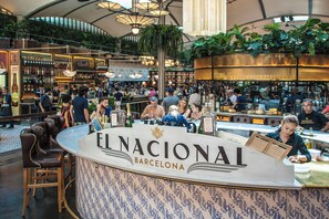 Un espace bar animé, avec un comptoir portant l’inscription « EL NACIONAL BARCELONA » et différents types de sièges.