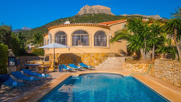 Zona de piscina con sillas de descanso, una mesa y vistas a la montaña.