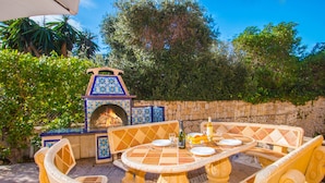 Un patio al aire libre con pared de piedra, mesa con azulejos y sillas con cojines amarillos.